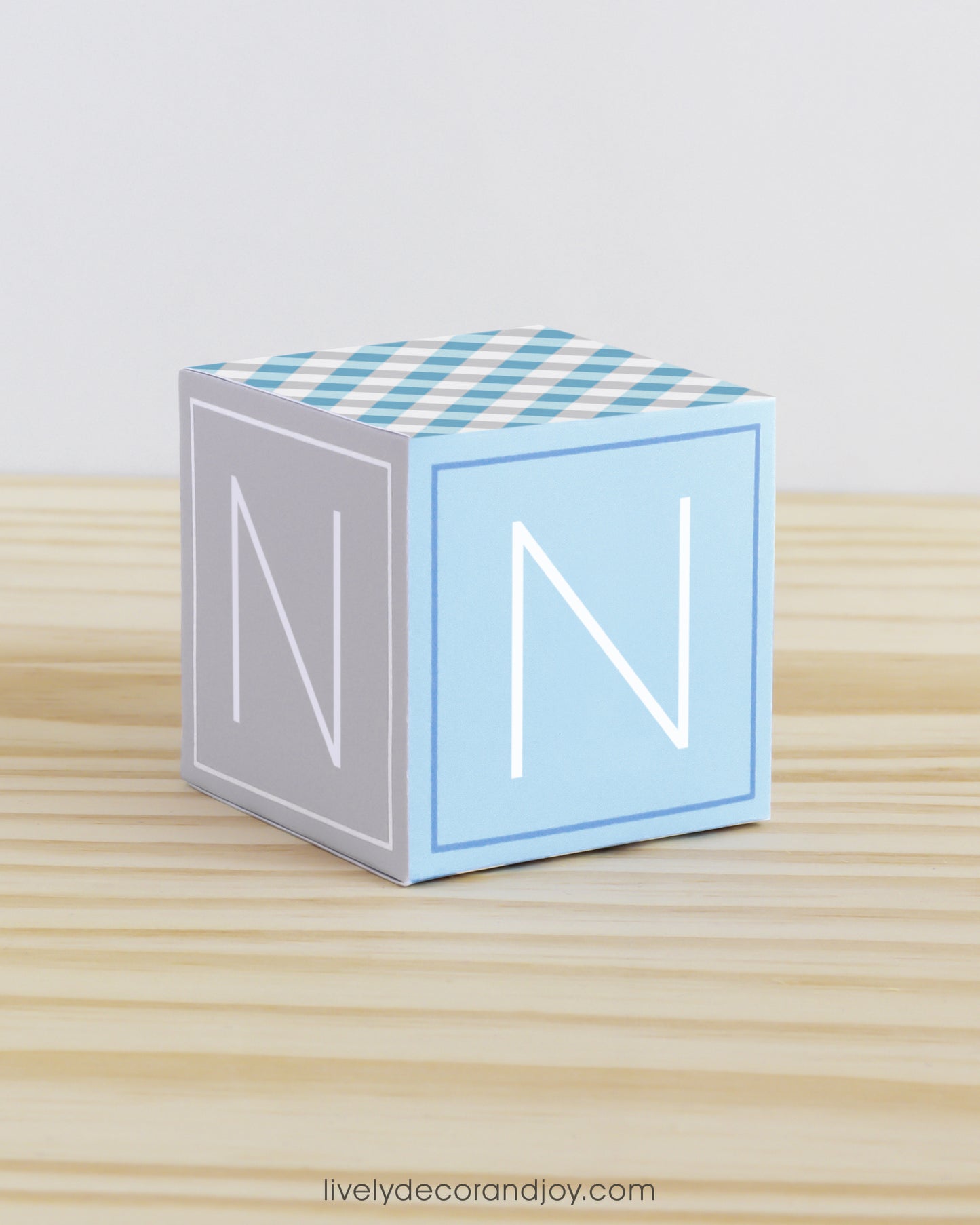 On a wooden table is a paper building block in tints of blue and light grey. Has the letter N on the sides.