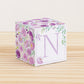 On a wooden table is a paper building block with purple and green floral designs and the letter N in lavender on the front.