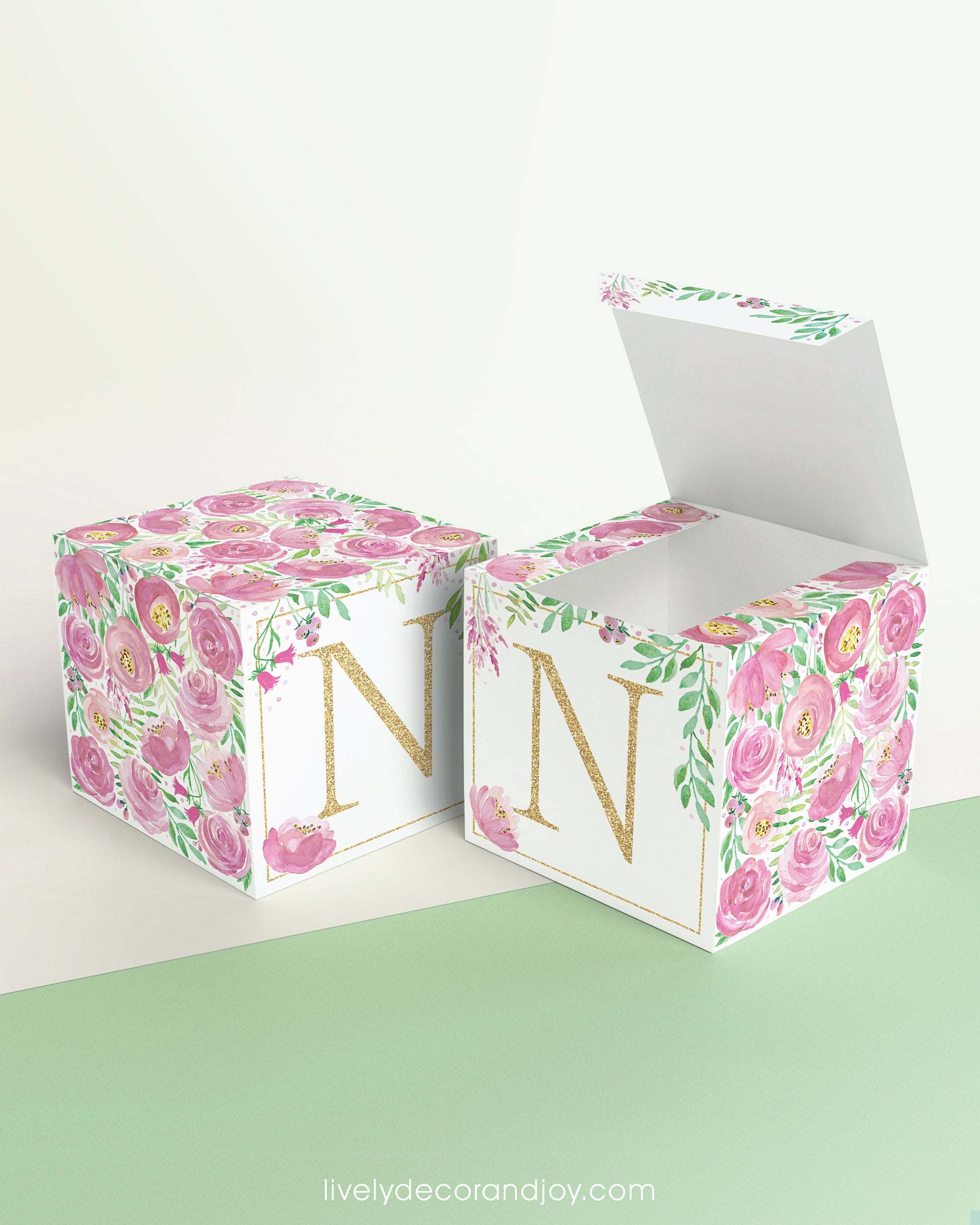 Two paper cubes with pink floral designs and the letter N in gold. One has the top open, showing it can be a cube or a box.