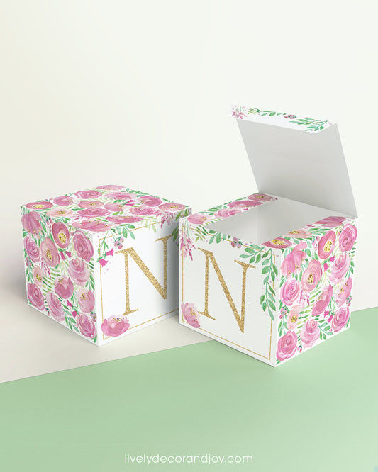 Two paper cubes with pink floral designs and the letter N in gold. One has the top open, showing it can be a cube or a box.