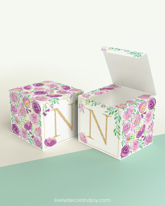 Two paper cubes with purple floral designs and the letter N in gold. One has the top open, showing it can be a cube or a box.