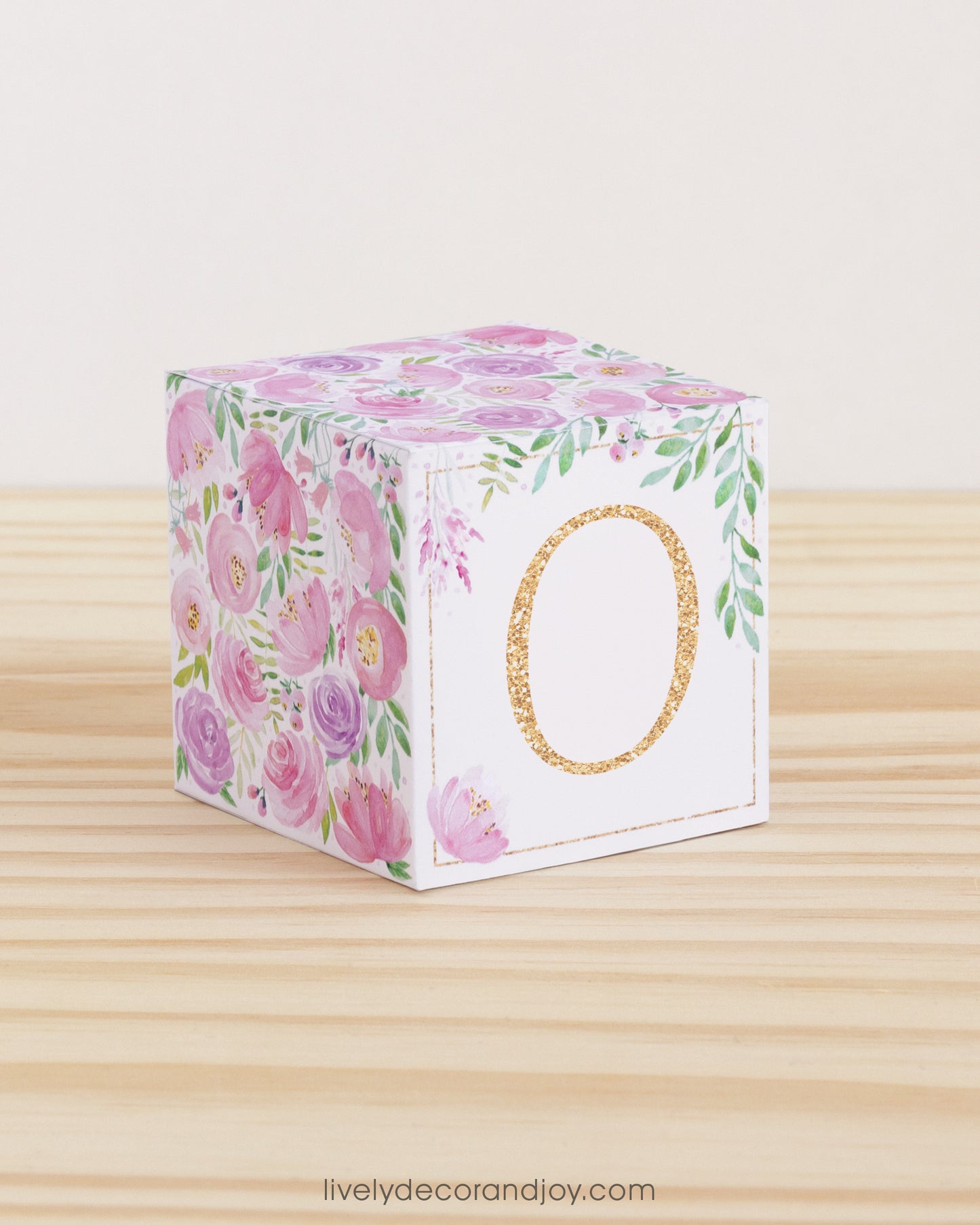 Baby block with blush and lavender floral designs and a peach letter O is on a wooden surface. It is a paper building block.