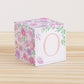 Baby block with blush and lavender floral designs and a peach letter O is on a wooden surface. It is a paper building block.