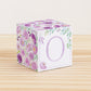 Baby block with purple and green floral designs and a lavender letter O is on a wooden surface. It is a paper building block.
