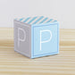 Paper building block in tints of blue and light grey. It has the letter P on the sides and is on a wood table or shelf.