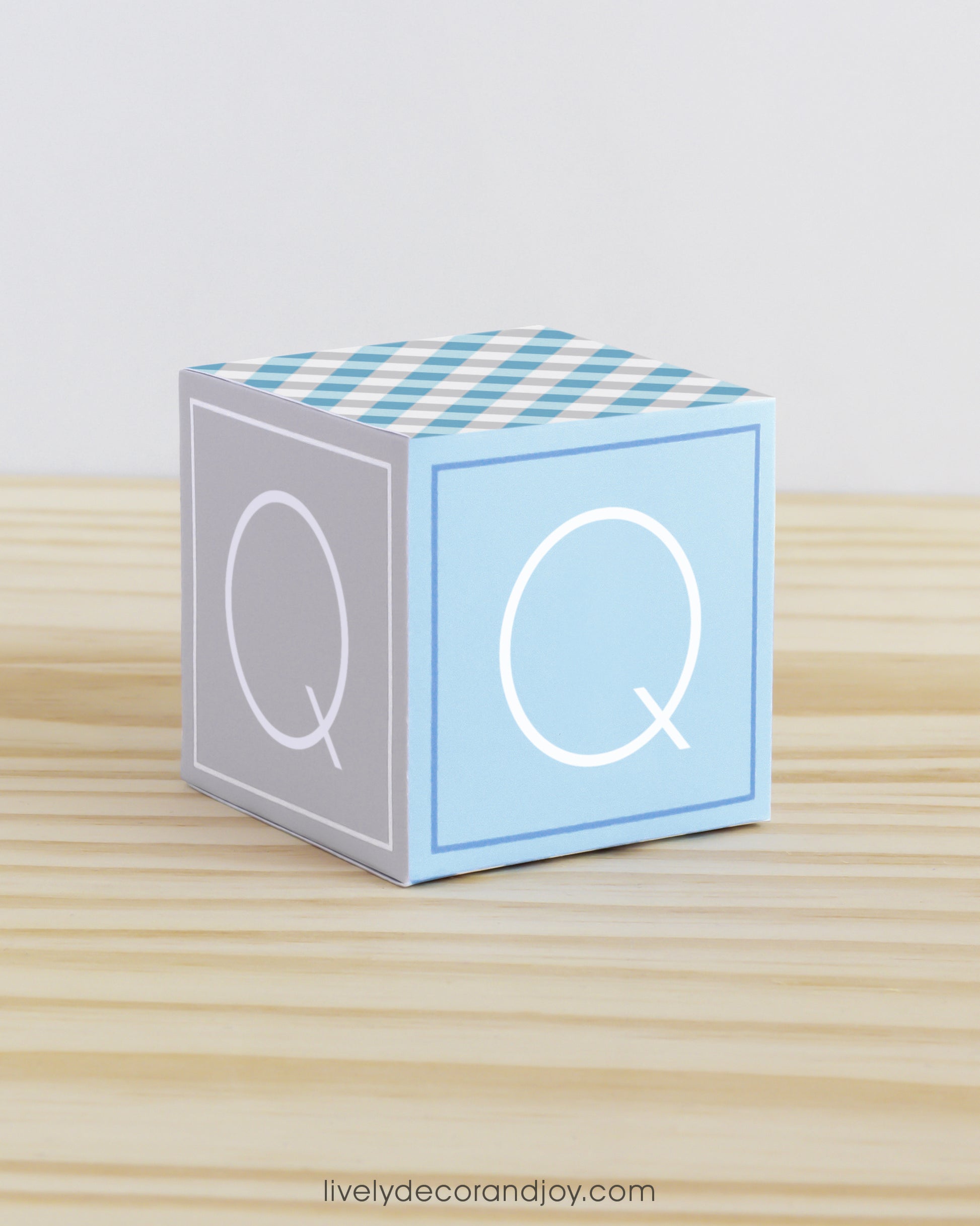 Letter block in blue and grey with the letter Q on the sides. It is made of paper.