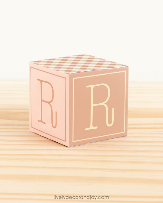 Paper building block in farmhouse colors. It has the letter R on the sides and is on a wood table or shelf.