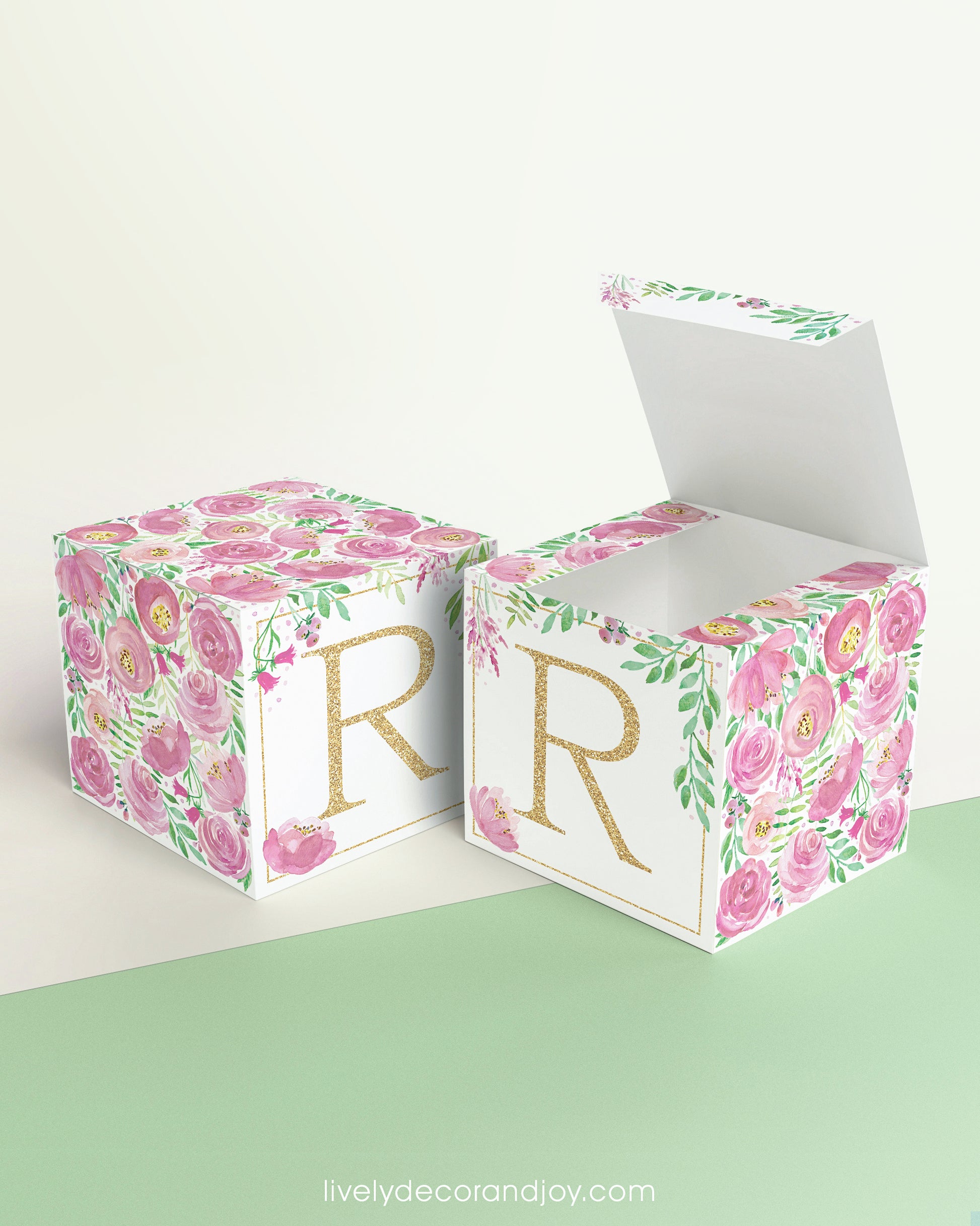 Two identical paper cubes with printed floral designs and the letter R. One has the top open, showing that it is a box.