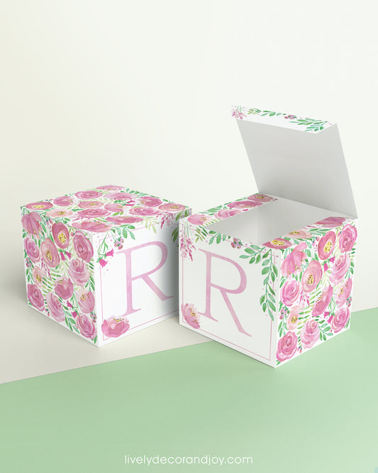 Two identical paper cubes with printed floral designs and the letter R. One has the top open, showing that it is a box.
