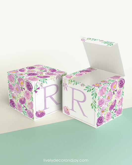 Two identical paper cubes with printed floral designs and the letter R. One has the top open, showing that it is a box.