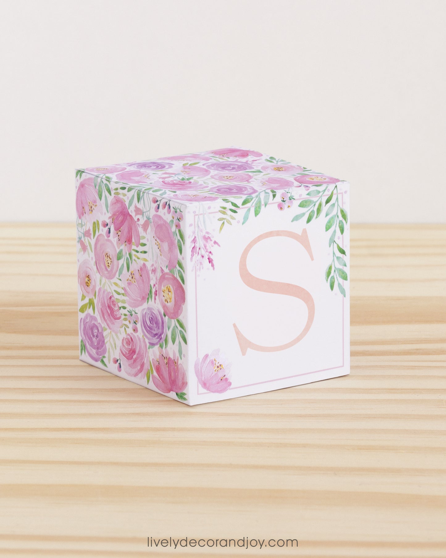 Building block made of printed paper with floral cottagecore designs and the letter S on the front. It is on a wooden table.