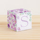 Building block made of printed paper with floral cottagecore designs and the letter S on the front. It is on a wooden table.