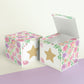 Paper building block with floral designs and a star on the front shown both as a cube and as an open box.