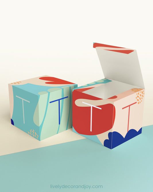Two identical paper cubes with abstract printed designs and the letter T. One has the top open, showing that it is a box.