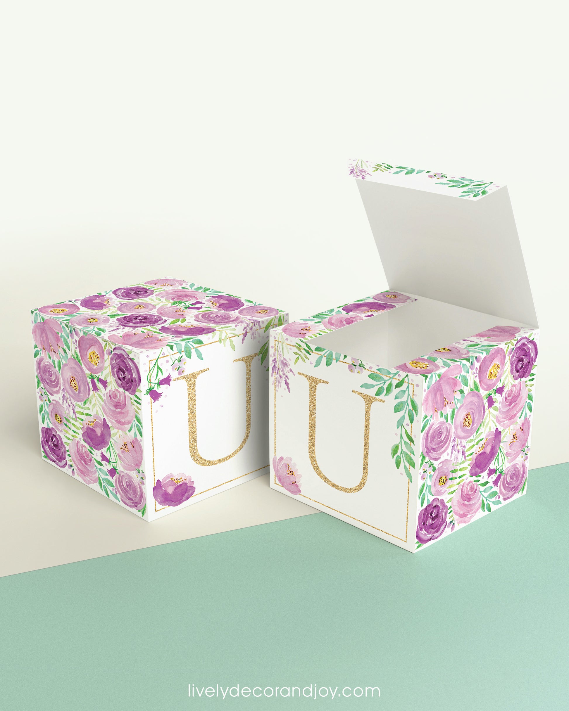 Two printed DIY paper cubes have the same designs, one of which has an open lid, showing that it is a box.