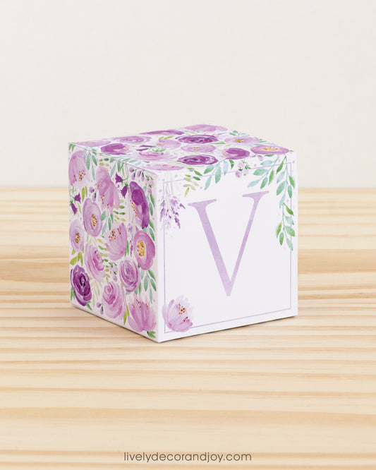 Paper building block features watercolor flowers and leaves in purple and green. Has a lavender letter V on the front.