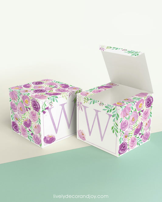 Two blocks made of paper, one has the top lid open. Floral designs cover all sides except the front, which has the letter W.