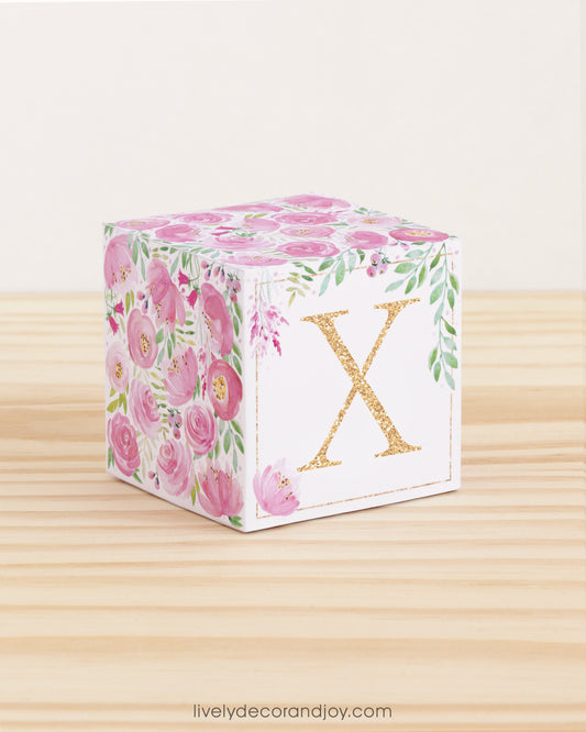 Paper cube with printed boho floral motifs and the letter X on the front. It features pink and green flowers and leaves.