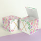 Two identical paper cubes with printed floral designs and the letter X. One has the top open, showing that it is a box.