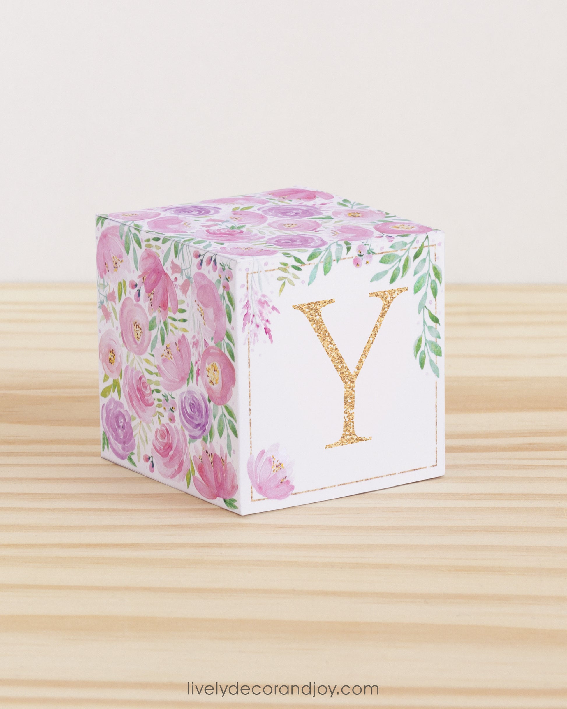 Building block made of printed paper with floral cottagecore designs and the letter Y on the front. It is on a wooden table.