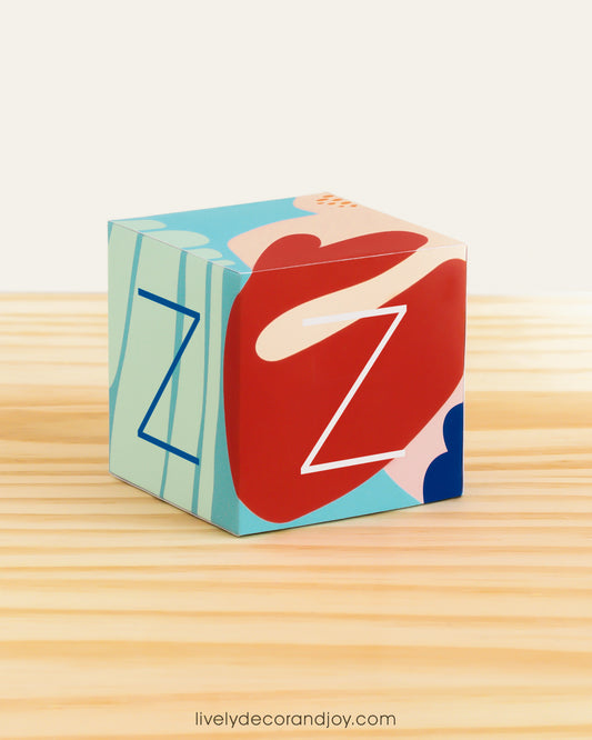 Paper building block in coral reef colors. It has the letter Z on the sides and is on a wood table or shelf.