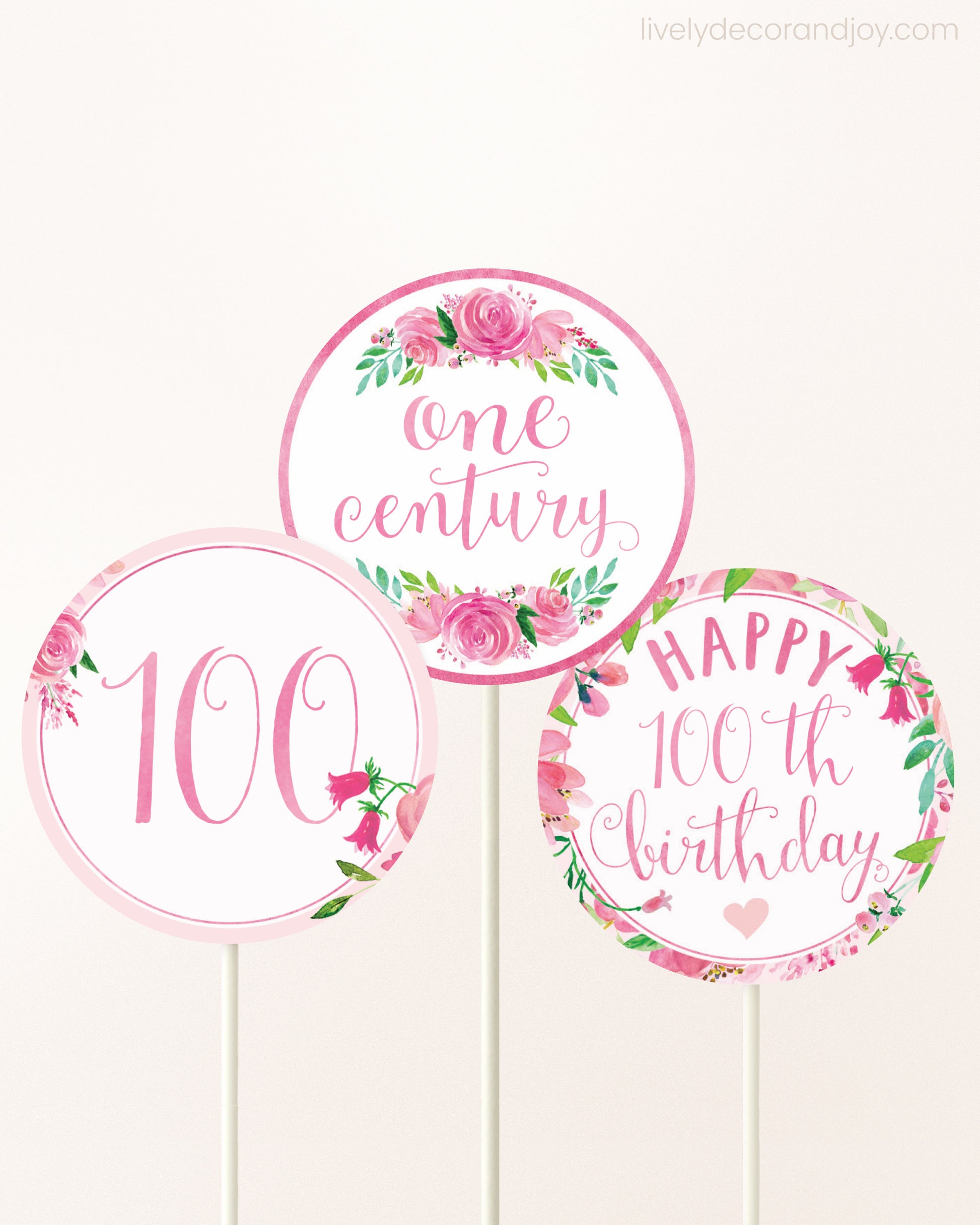 Three cupcakes toppers attached to lollipop sticks. They feature pink watercolor floral designs and pink and gold handwritten text.