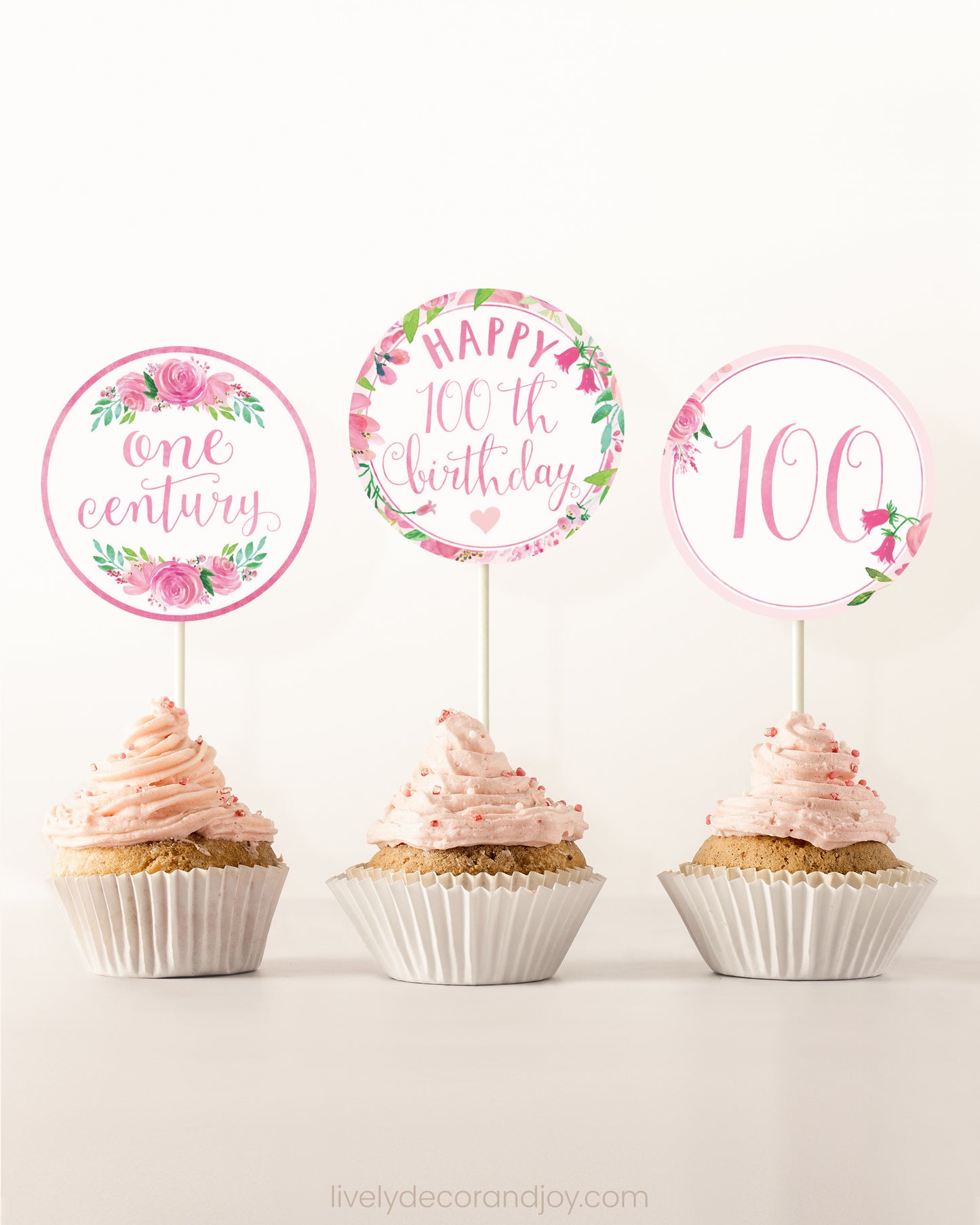 Three cupcakes on a dessert table. Each has a round cupcake topper with pink watercolor floral designs and pink and gold letters.