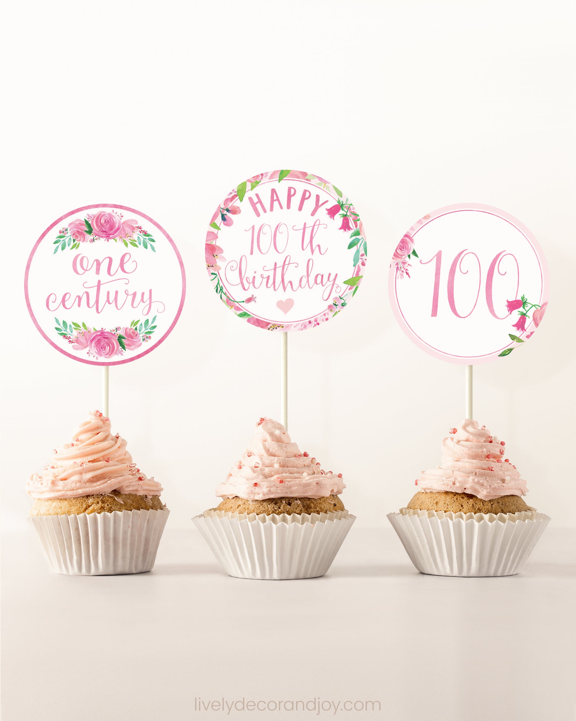 Three cupcakes on a dessert table. Each has a round cupcake topper with pink watercolor floral designs and pink and gold letters.