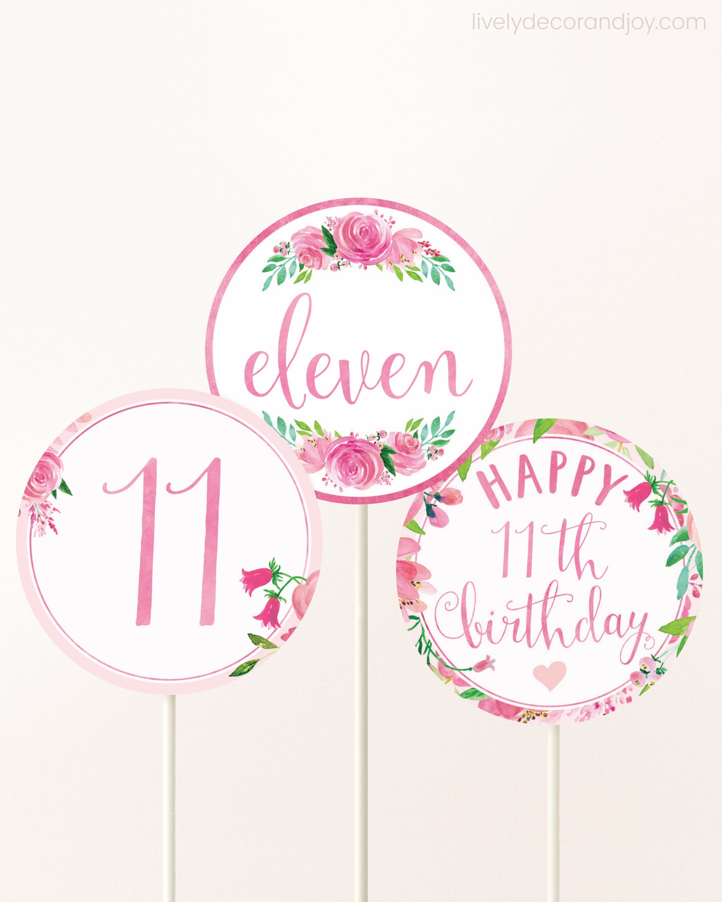 Three DIY toppers attached to lollipop sticks. They show printable cupcake topper designs with pink watercolor flowers.