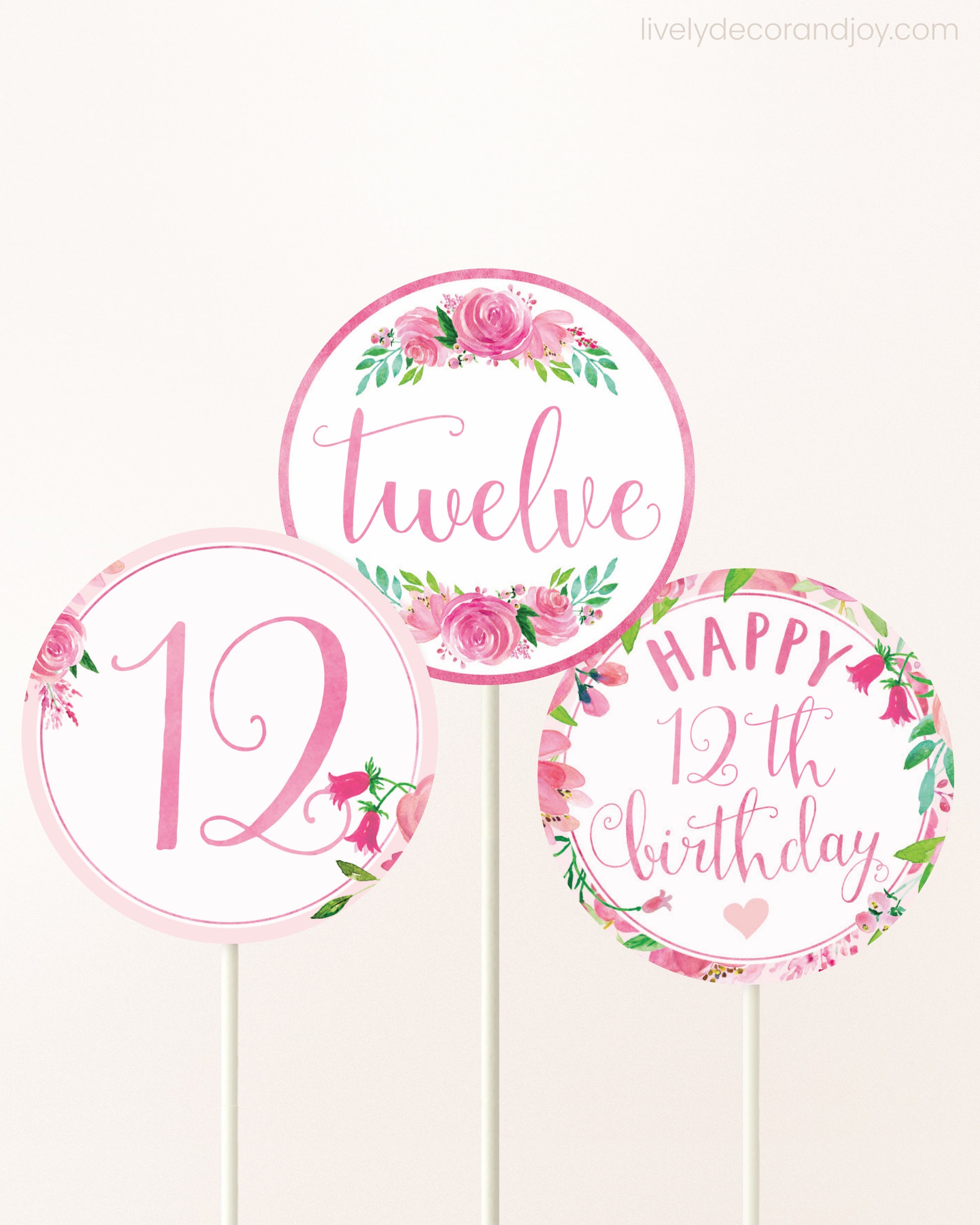 Three cupcakes toppers attached to lollipop sticks. They feature pink watercolor floral designs and pink and gold handwritten text.