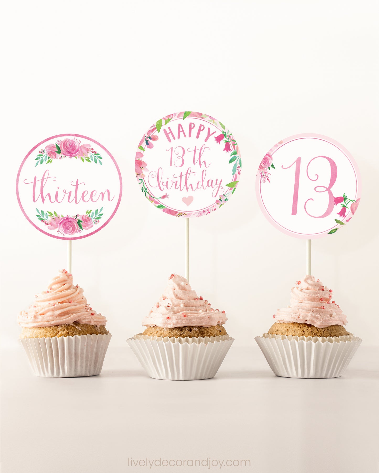 Three cupcakes side by side. Each has a round cupcake topper with pink watercolor flowers and pink and gold letters.