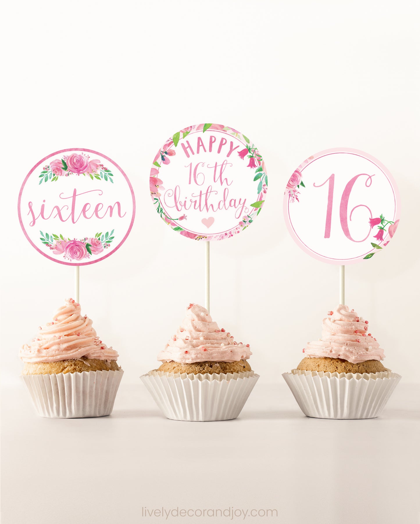 Three cupcakes side by side. Each has a round cupcake topper with pink watercolor flowers and pink and gold letters.