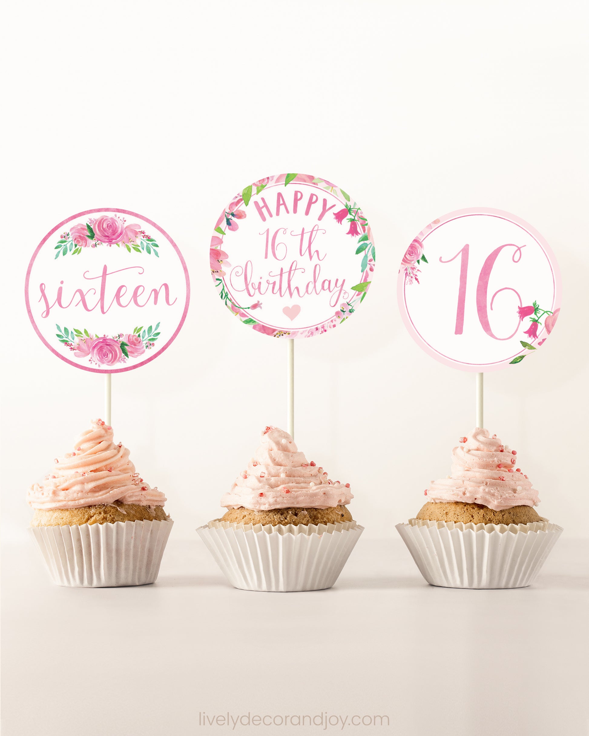 Three cupcakes side by side. Each has a round cupcake topper with pink watercolor flowers and pink and gold letters.