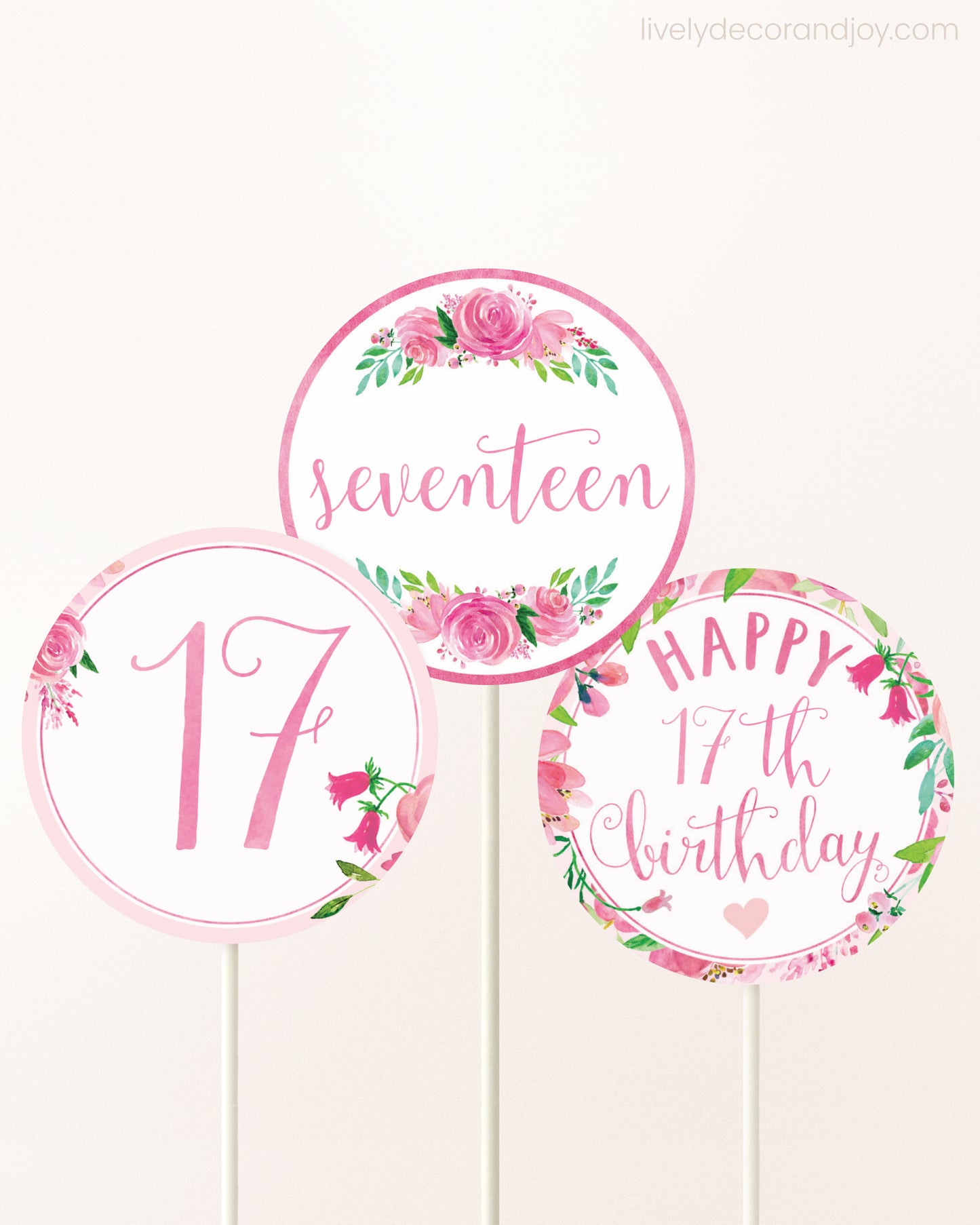 Three cupcakes toppers attached to lollipop sticks. They feature pink watercolor floral designs and pink and gold handwritten text.