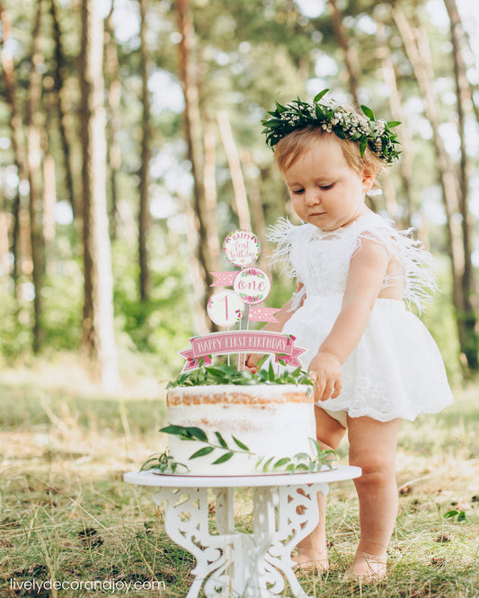 A cute little girl next to her healthy smash cake in a park. It is a rustic sponge cake with a printed cake topper.