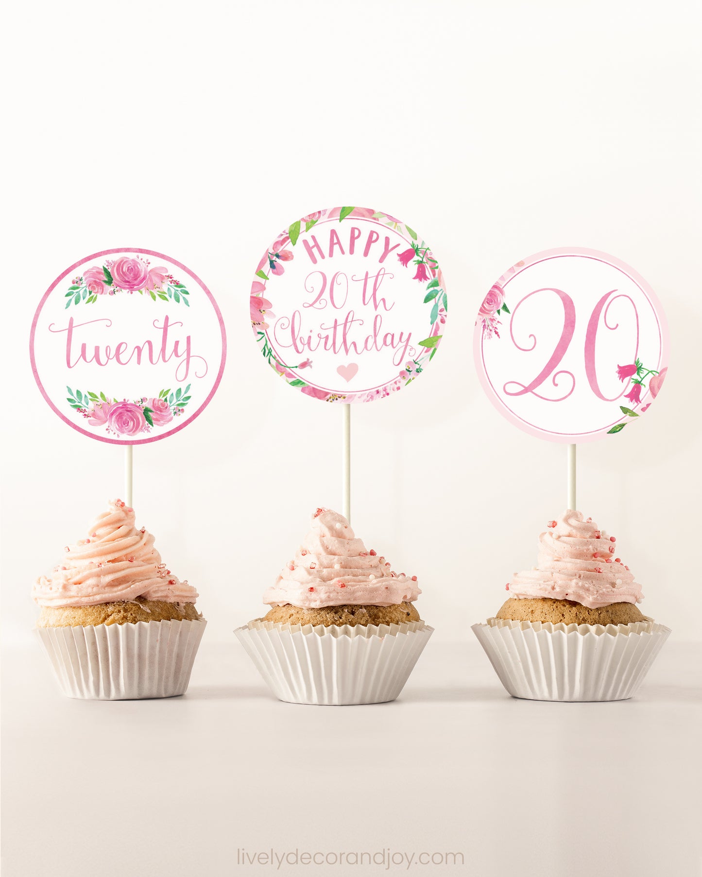 Three cupcakes on a dessert table. Each has a round cupcake topper with pink watercolor floral designs and pink and gold letters.