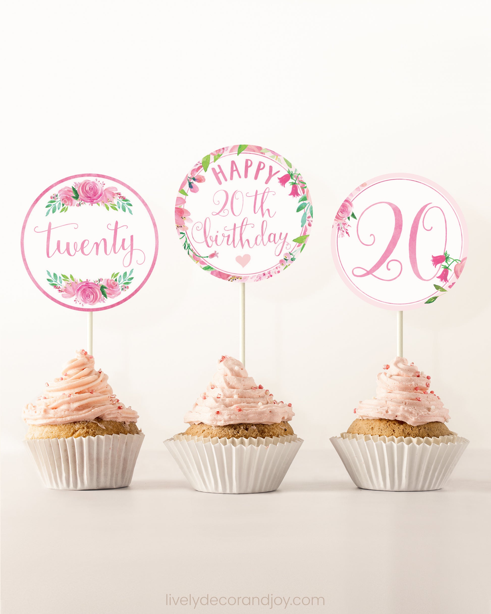 Three cupcakes on a dessert table. Each has a round cupcake topper with pink watercolor floral designs and pink and gold letters.