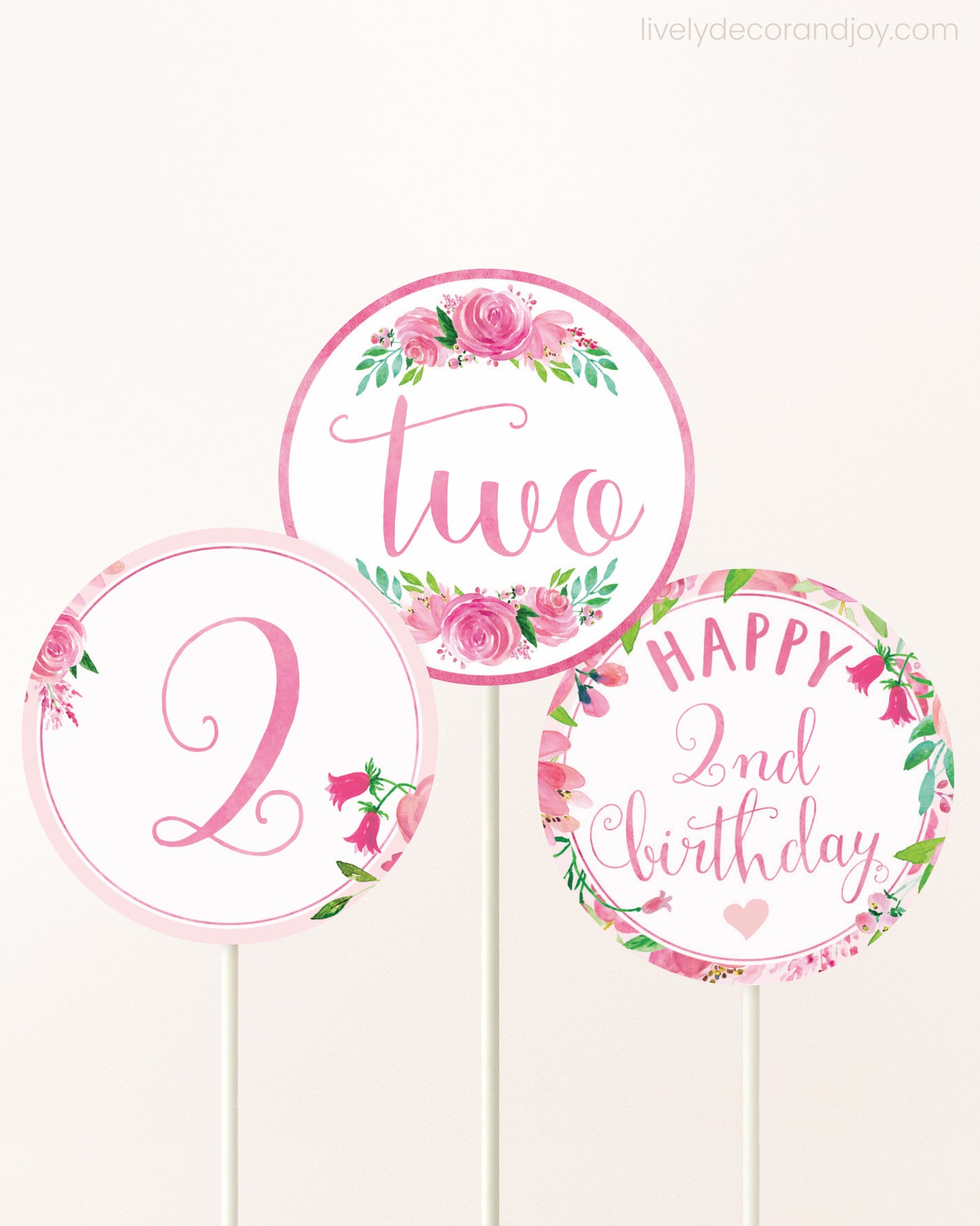 Three cupcakes toppers attached to lollipop sticks. They feature pink watercolor floral designs and pink and gold handwritten text.