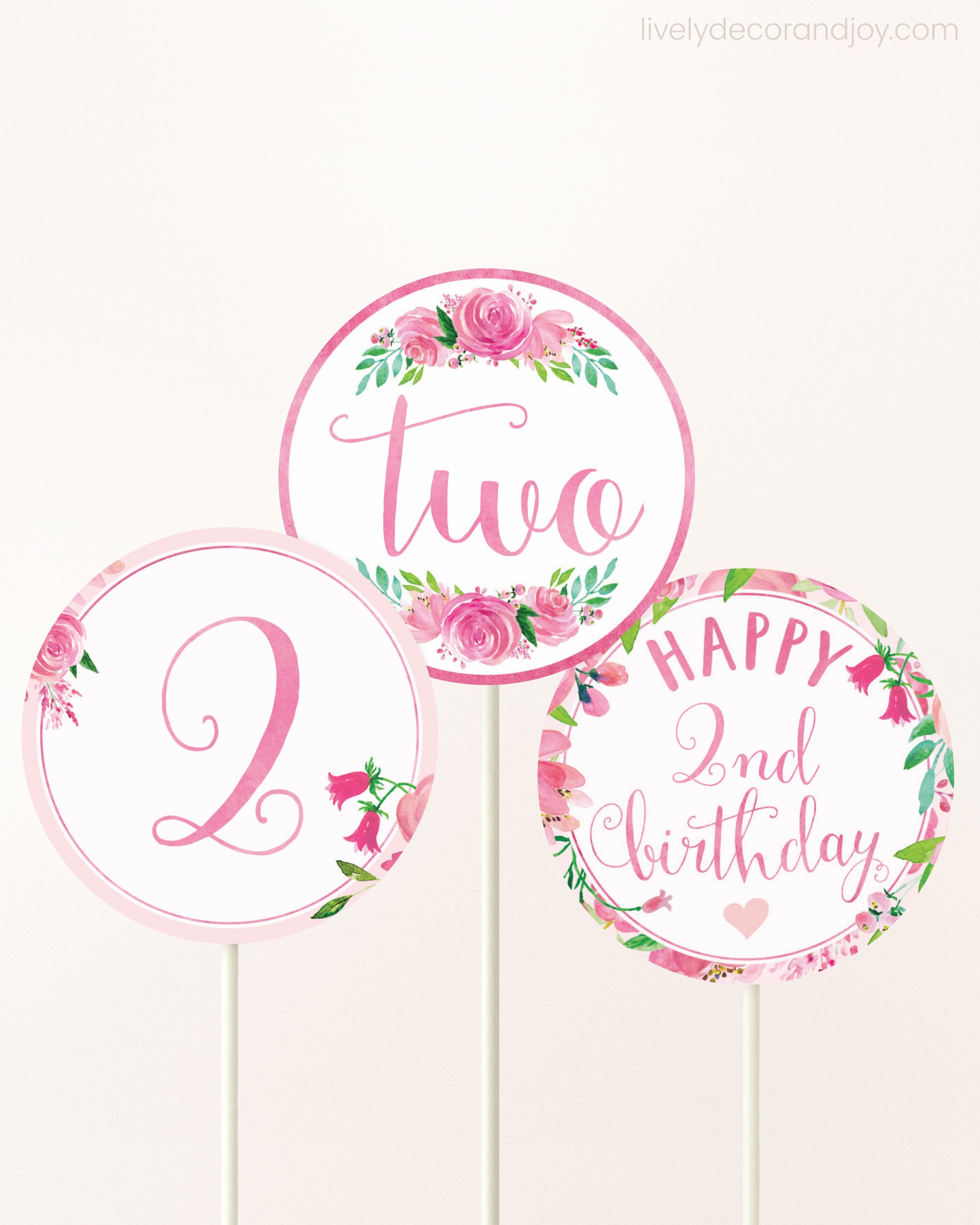 Three cupcakes toppers attached to lollipop sticks. They feature pink watercolor floral designs and pink and gold handwritten text.