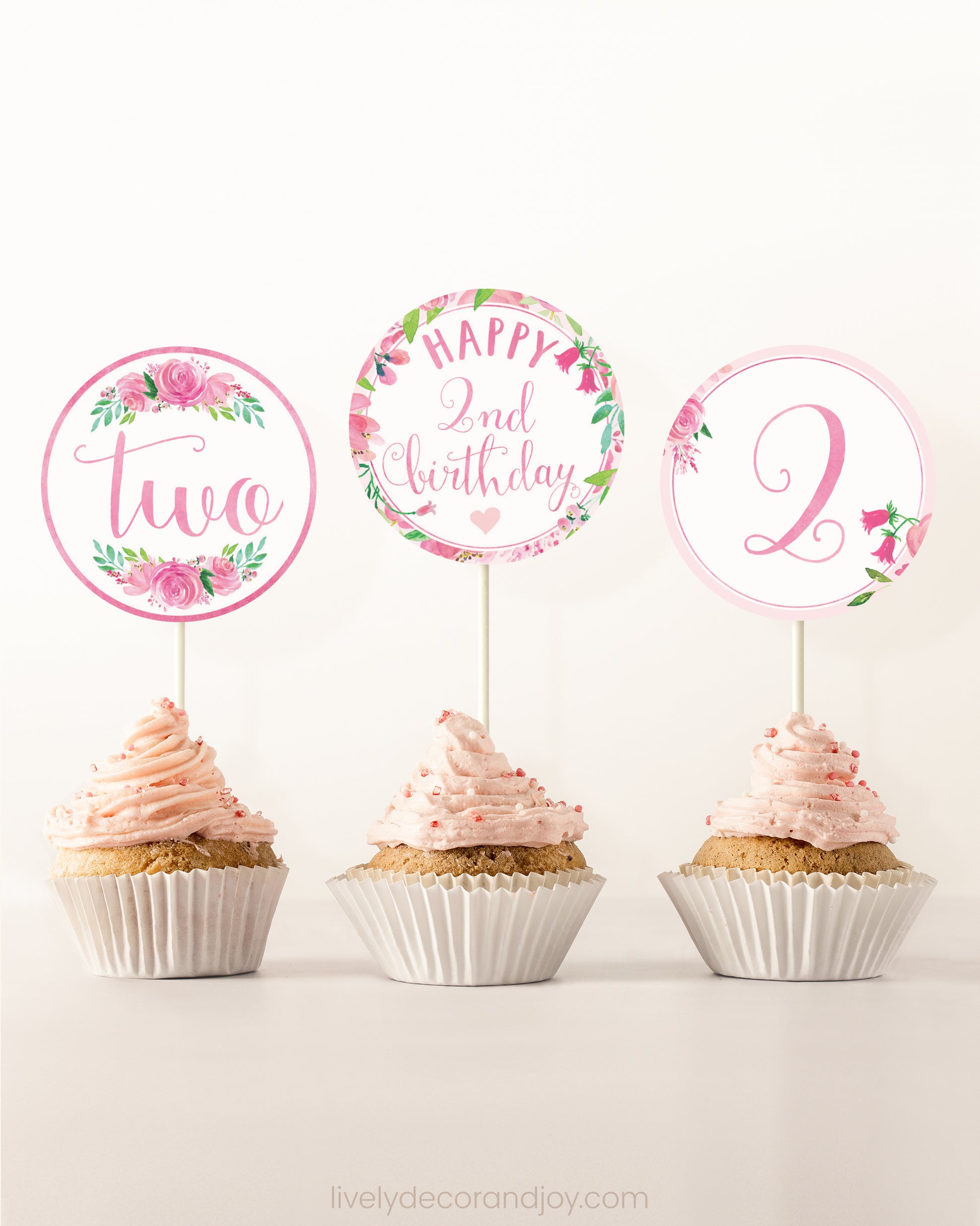 Three cupcakes on a dessert table. Each has a round cupcake topper with pink watercolor floral designs and pink and gold letters.