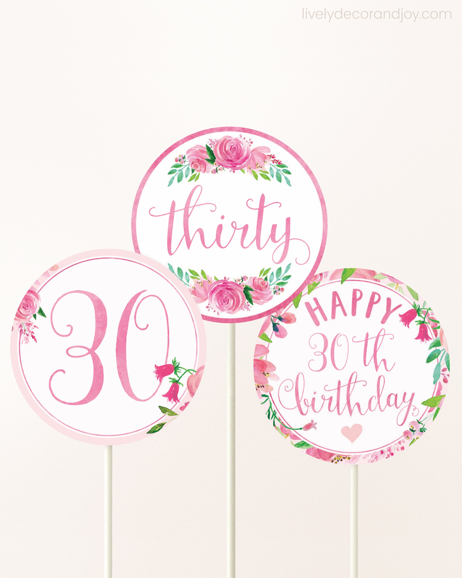 Three cupcakes toppers attached to lollipop sticks. They feature pink watercolor floral designs and pink and gold handwritten text.