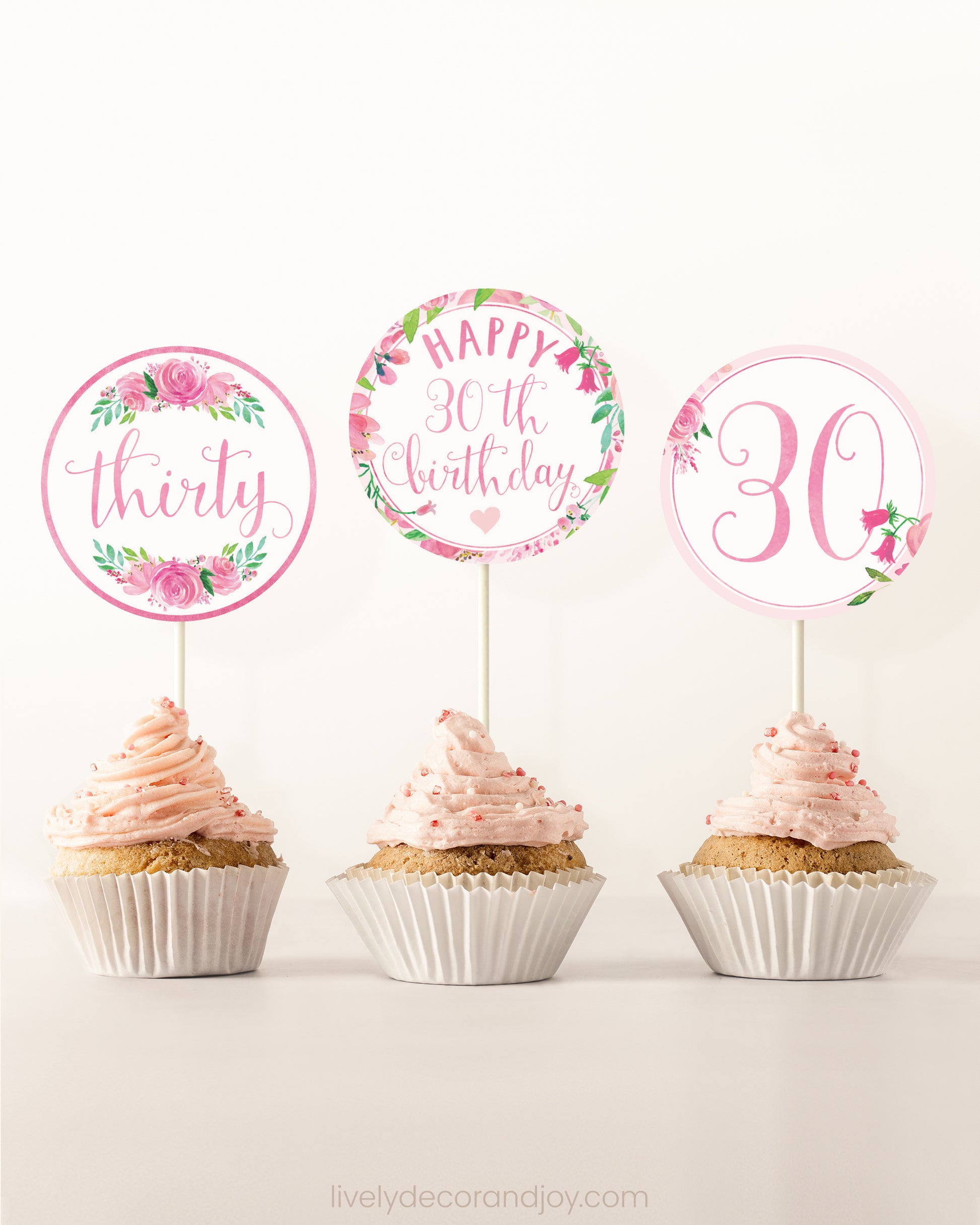Three cupcakes on a dessert table. Each has a round cupcake topper with pink watercolor floral designs and pink and gold letters.