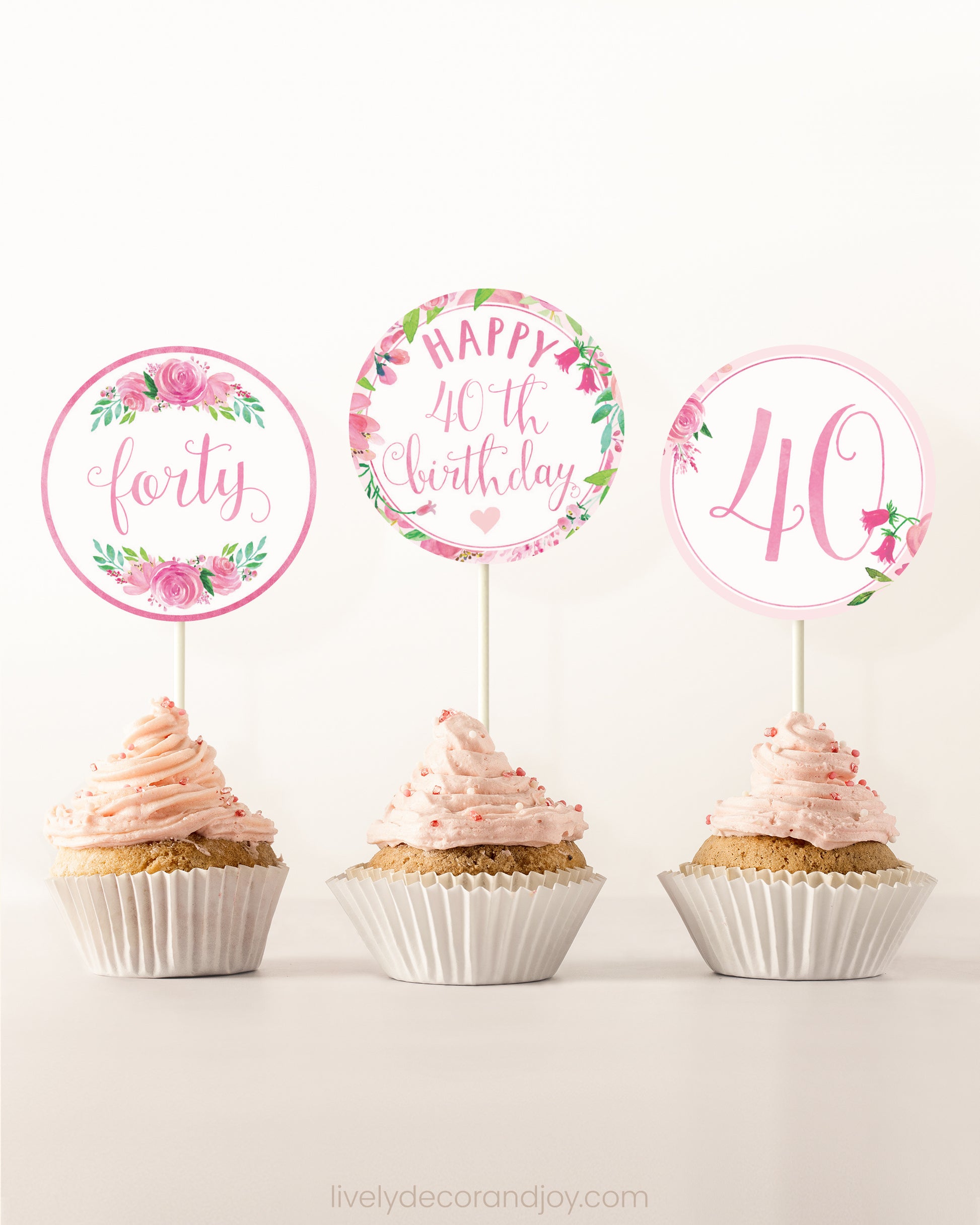 Three cupcakes side by side. Each has a round cupcake topper with pink watercolor flowers and pink and gold letters.
