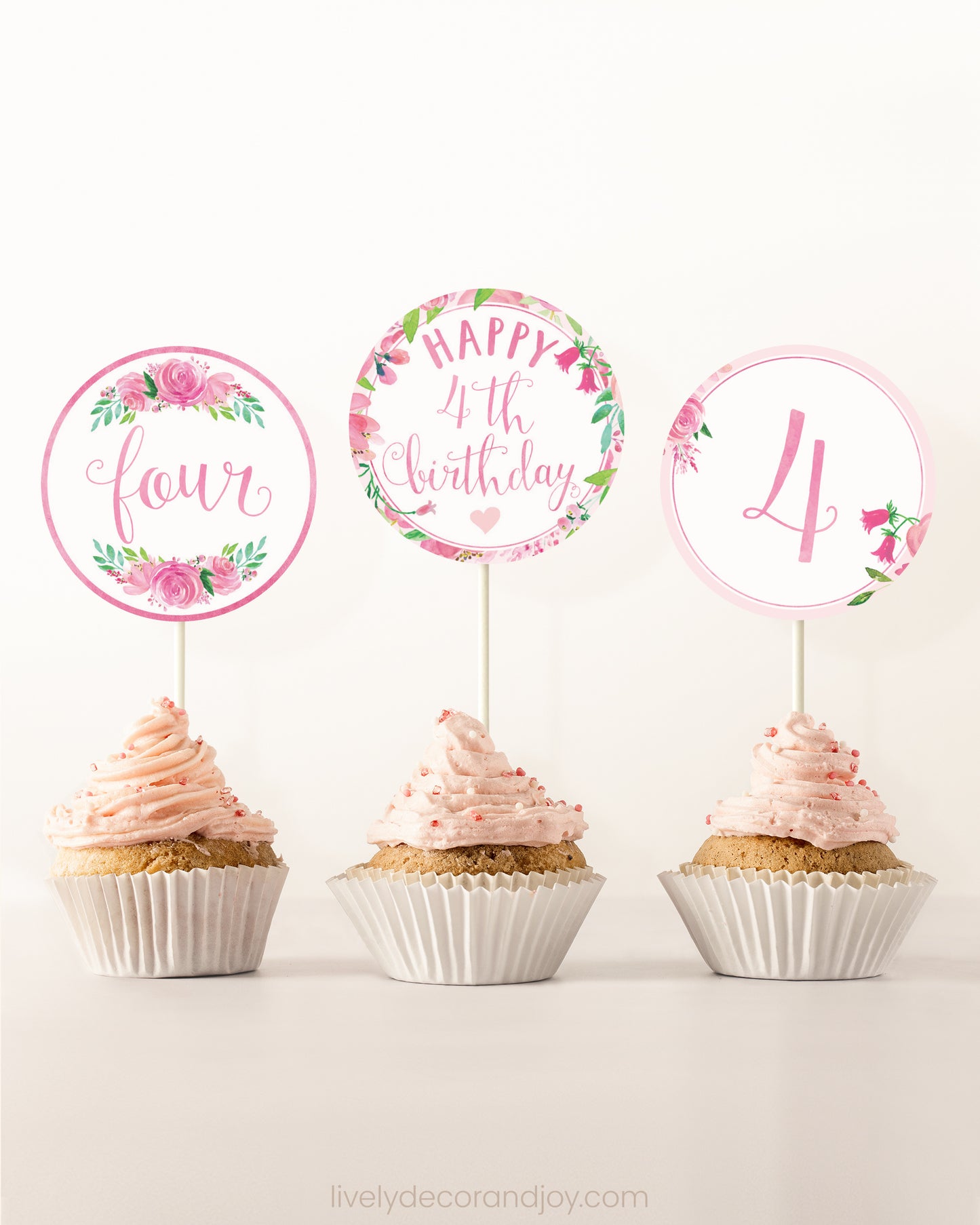 Three cupcakes on a dessert table. Each has a round cupcake topper with pink watercolor floral designs and pink and gold letters.