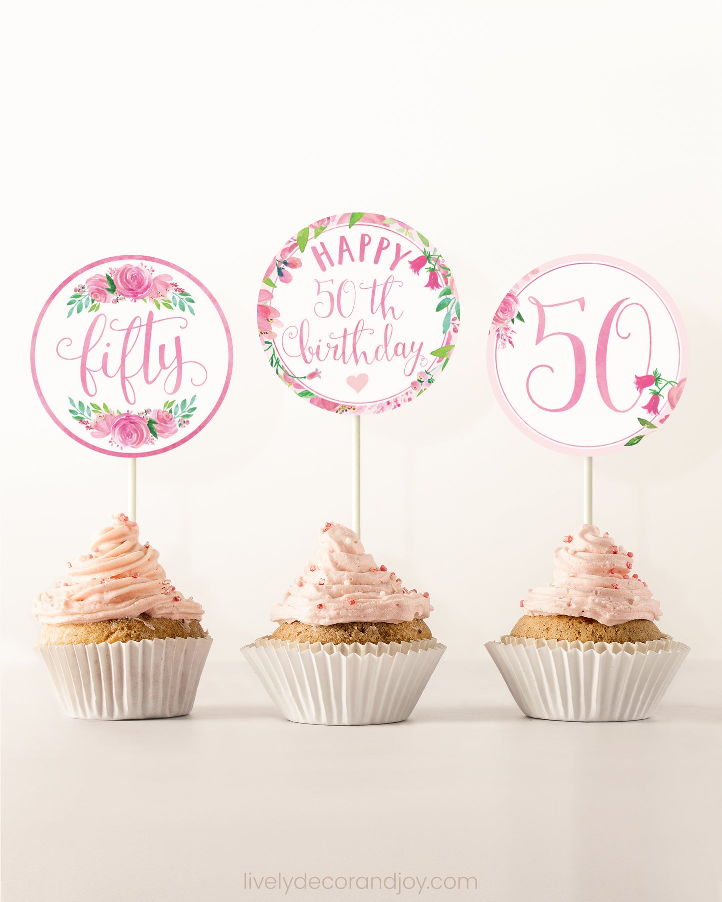 Three cupcakes side by side. Each has a round cupcake topper with pink watercolor flowers and pink and gold letters.