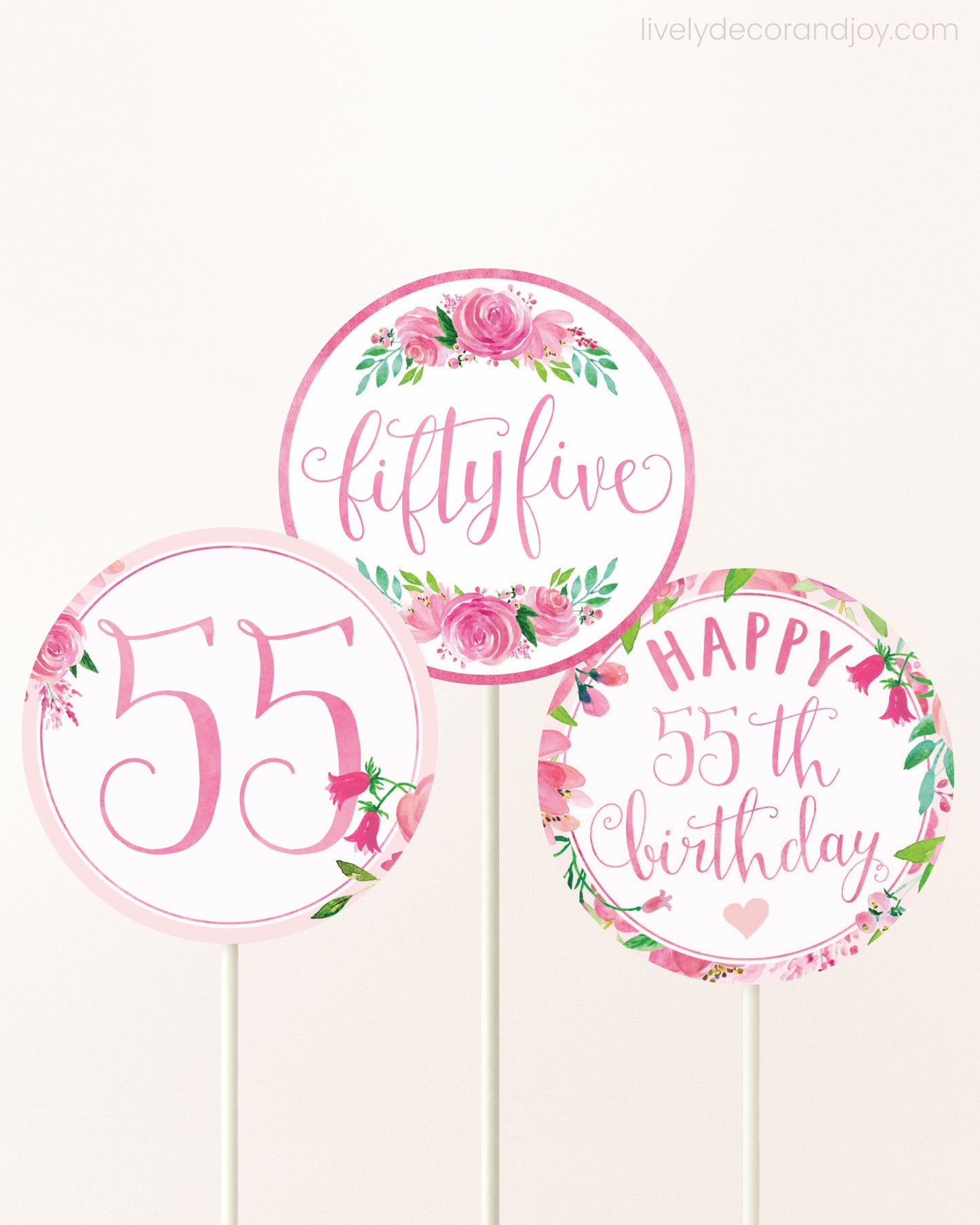 Three cupcakes toppers attached to lollipop sticks. They feature pink watercolor floral designs and pink and gold handwritten text.