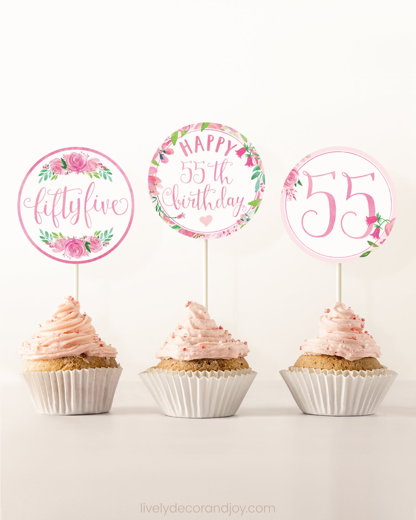 Three cupcakes on a dessert table. Each has a round cupcake topper with pink watercolor floral designs and pink and gold letters.