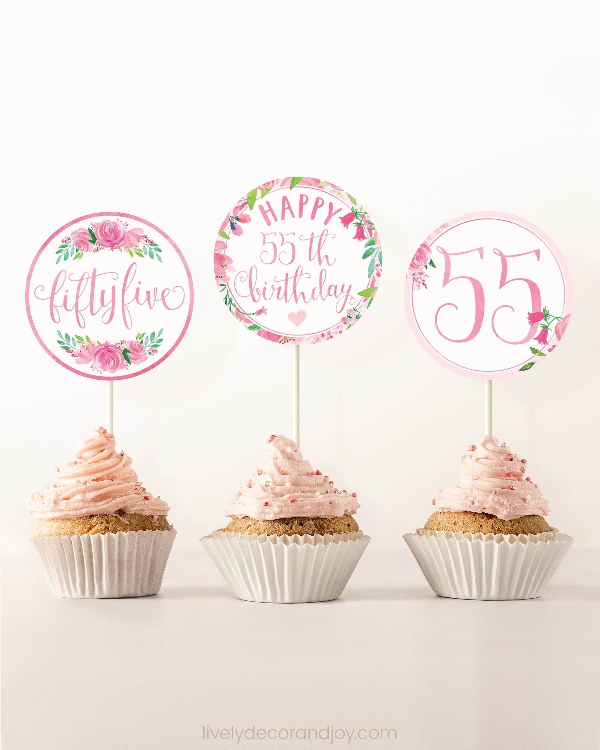 Three cupcakes on a dessert table. Each has a round cupcake topper with pink watercolor floral designs and pink and gold letters.