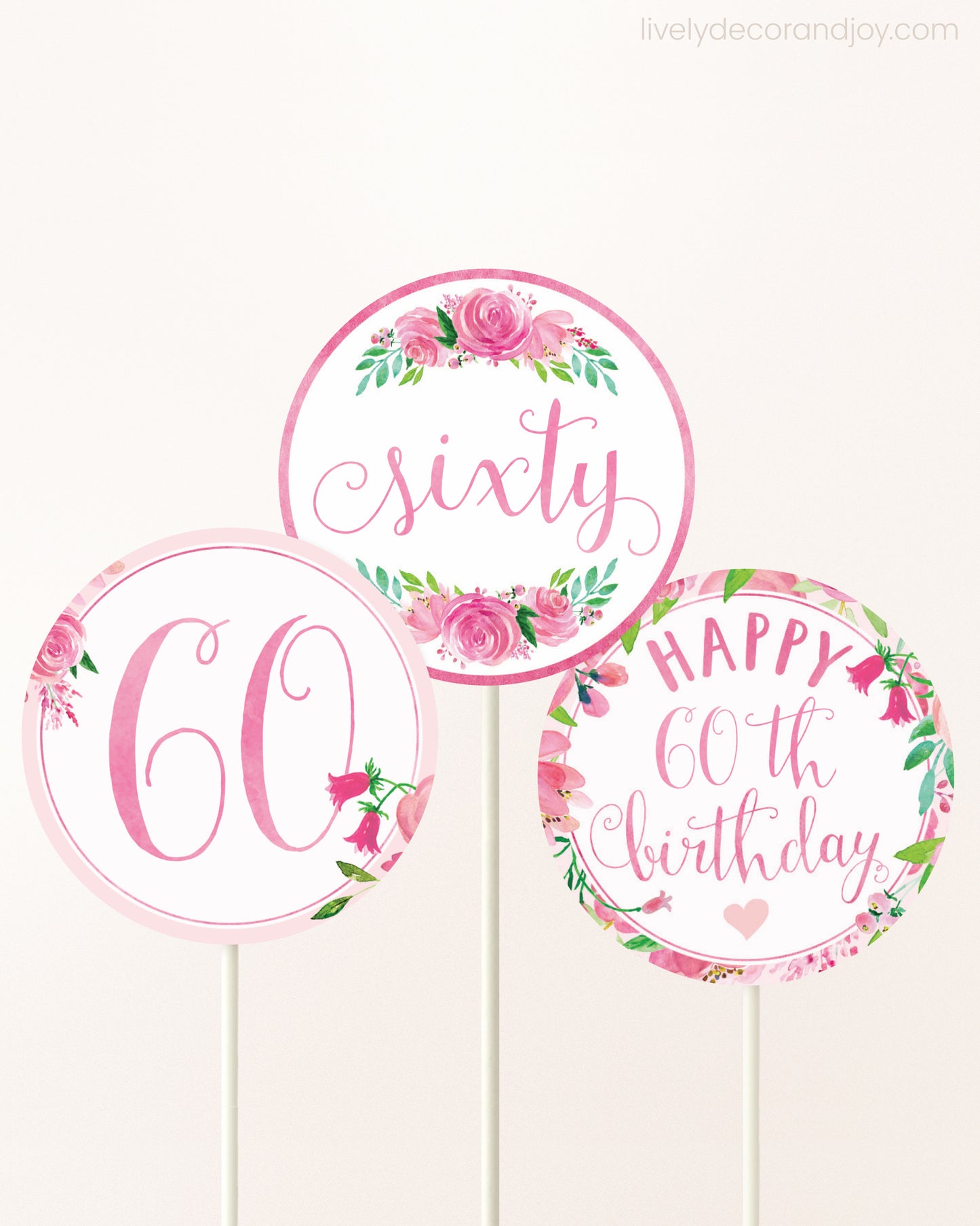 Three DIY toppers attached to lollipop sticks. They show printable cupcake topper designs with pink watercolor flowers.