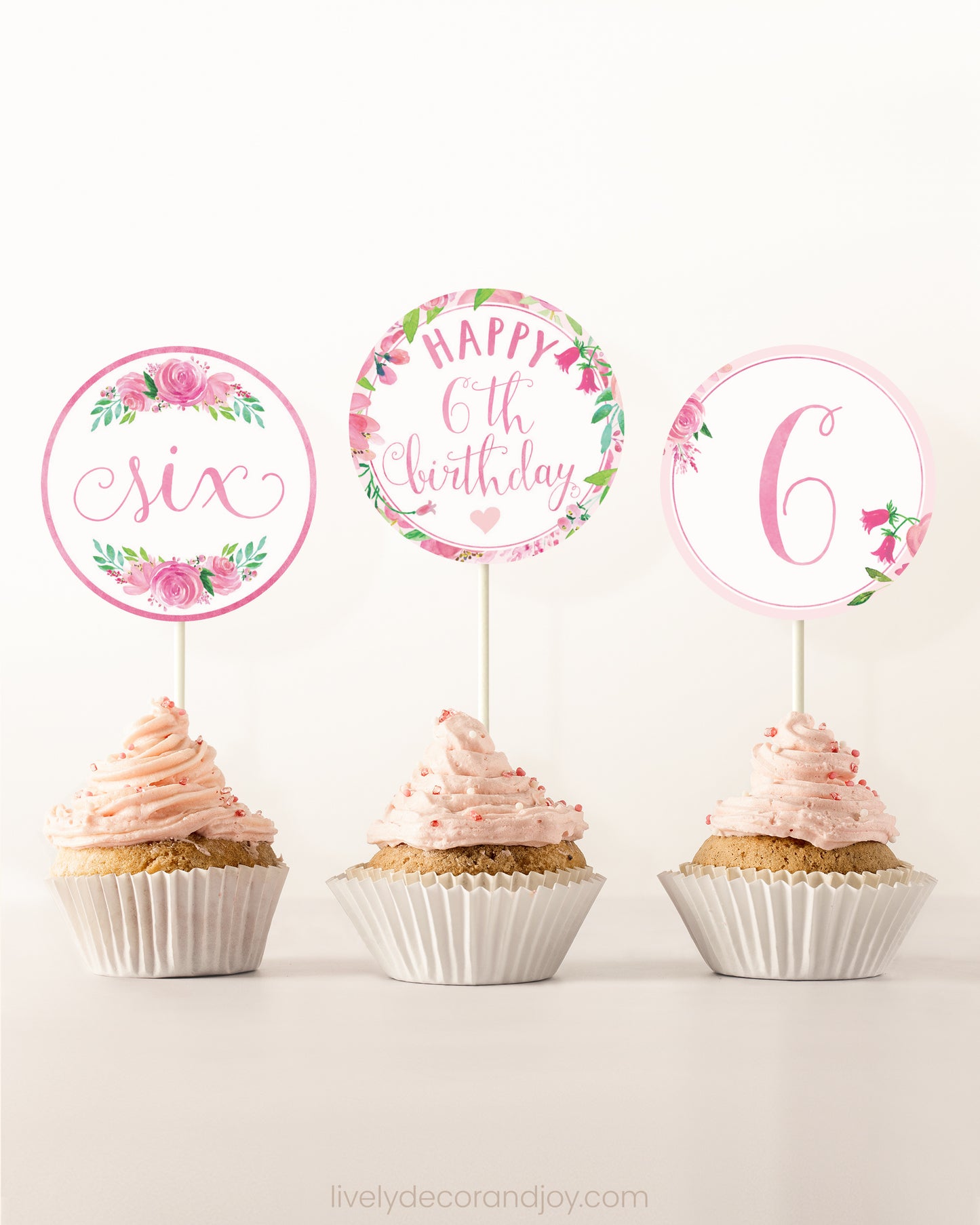 Three cupcakes on a dessert table. Each has a round cupcake topper with pink watercolor floral designs and pink and gold letters.